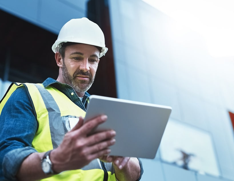 Man in hard hat and safety vest using a tablet.