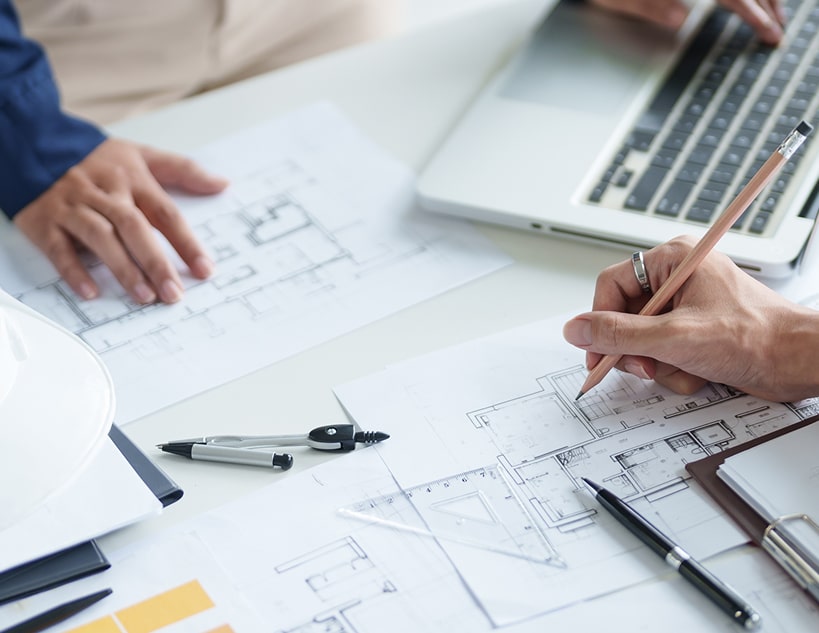 A close-up view of two individuals working on architectural drawings at a white table.