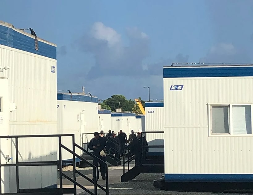 People gathered outside white and blue shipping containers.