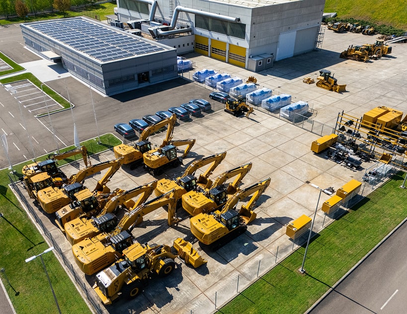 Aerial view of a fenced yard with yellow construction equipment and a warehouse.